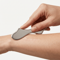 Hand gliding the Pluune steel scar massage stone over a pale line scar on a forearm