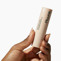 Closed Pluune silicone scar stick held upright between the fingers of one hand, white backdrop